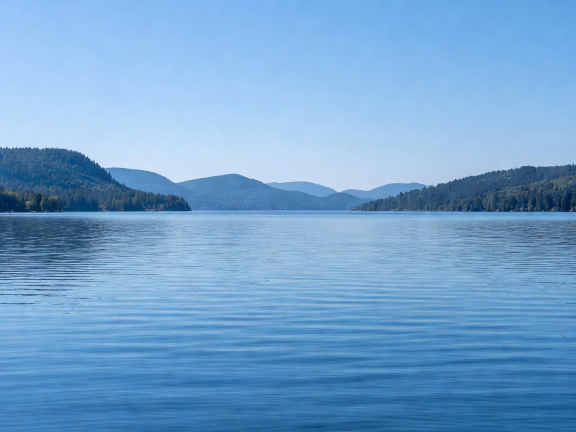 Expansive blue lake stretching to the horizon with distant forested hills